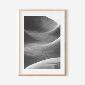 May include: Black and white photograph of a concrete skate park ramp. The ramp is curved and has a smooth surface. The photo is taken from a low angle, looking up at the ramp.