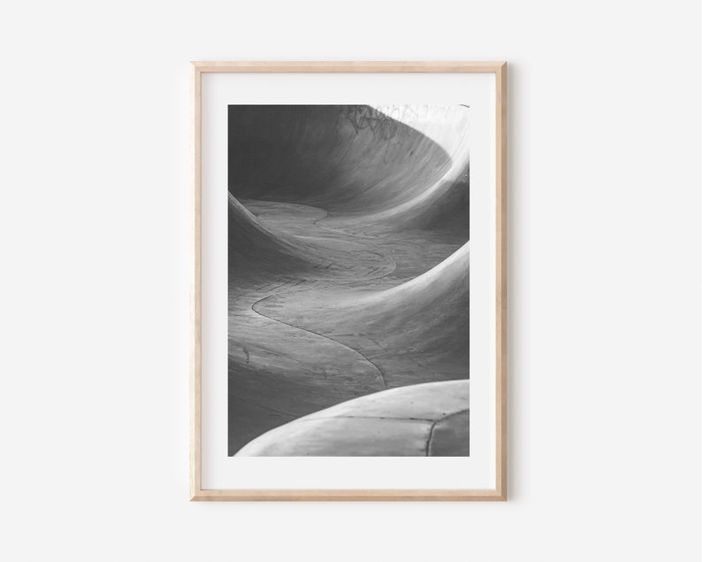 May include: Black and white photograph of a concrete skate park ramp. The ramp is curved and has a smooth surface. The photo is taken from a low angle, looking up at the ramp.