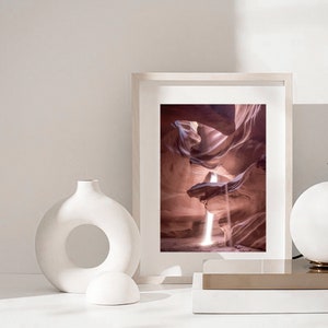 May include: A framed photograph of a canyon with a beam of light shining through the opening. The canyon walls are a reddish-brown color.