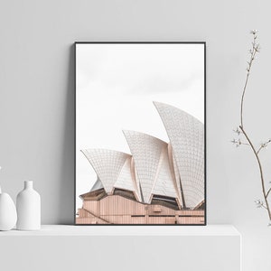 May include: A black framed print of the Sydney Opera House against a white background. The print is displayed on a white shelf with two white ceramic vases.