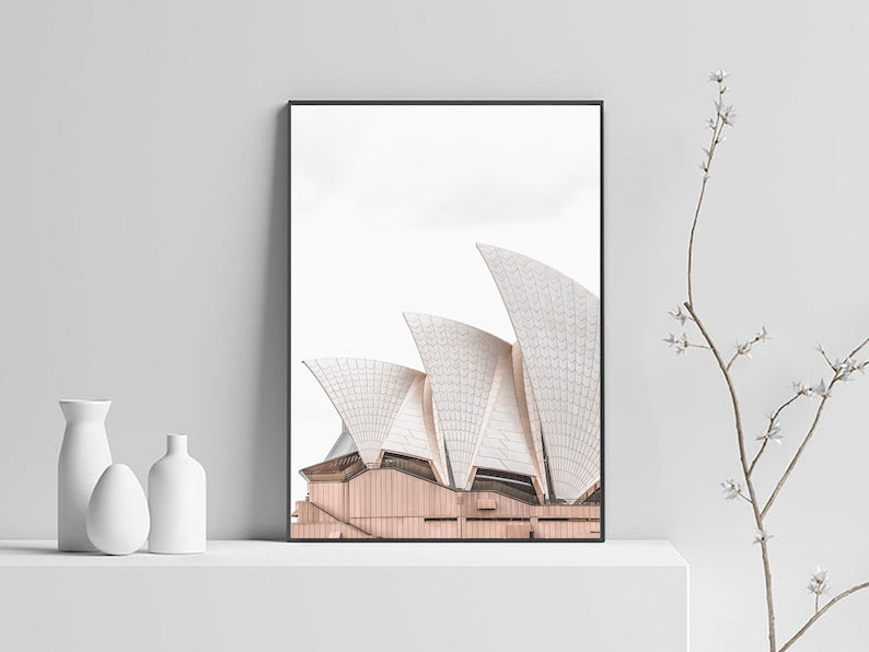 May include: A black framed print of the Sydney Opera House against a white background. The print is displayed on a white shelf with two white ceramic vases.