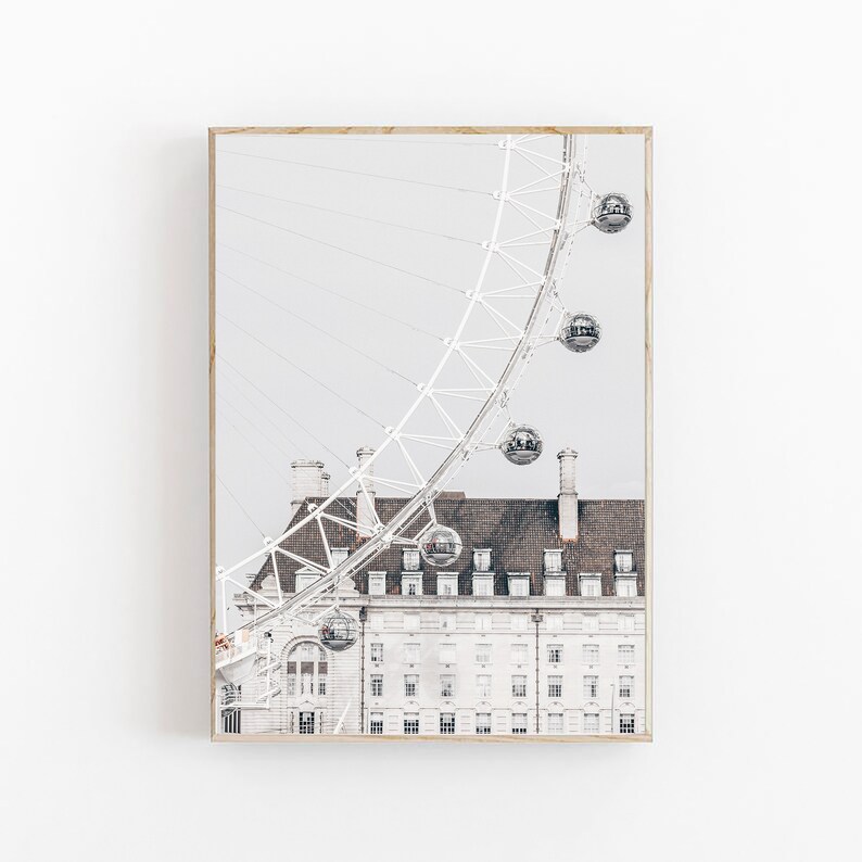 May include: A black and white photograph of the London Eye Ferris wheel partially obscured by a white building with brown accents. The Ferris wheel is in the background and the building is in the foreground. The Ferris wheel is a popular tourist attraction in London.