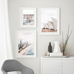 May include: Three framed photographs of different Australian landmarks. The top left photo shows a rocky coastline with ocean waves. The top right photo shows the Sydney Opera House. The bottom photo shows a cityscape with a beach.
