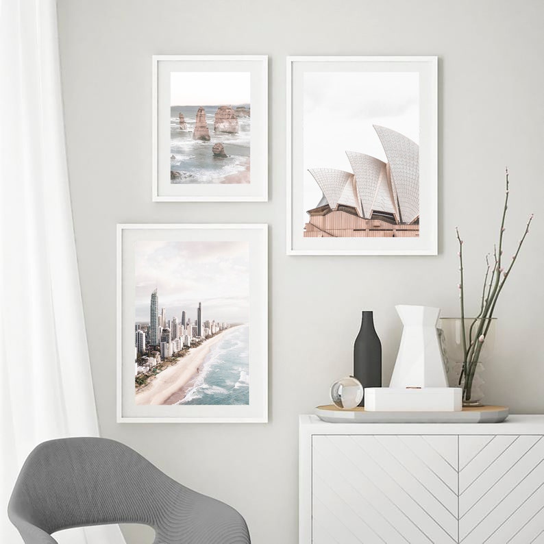May include: Three framed photographs of different Australian landmarks. The top left photo shows a rocky coastline with ocean waves. The top right photo shows the Sydney Opera House. The bottom photo shows a cityscape with a beach.