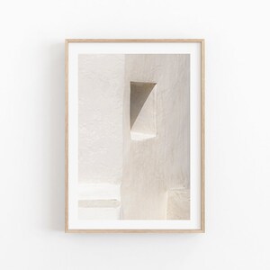 May include: Framed art print depicting an abstract architectural detail. The image shows a textured, off-white wall with a triangular opening. The artwork is presented in a light-coloured wooden frame, suitable for minimalist decor.