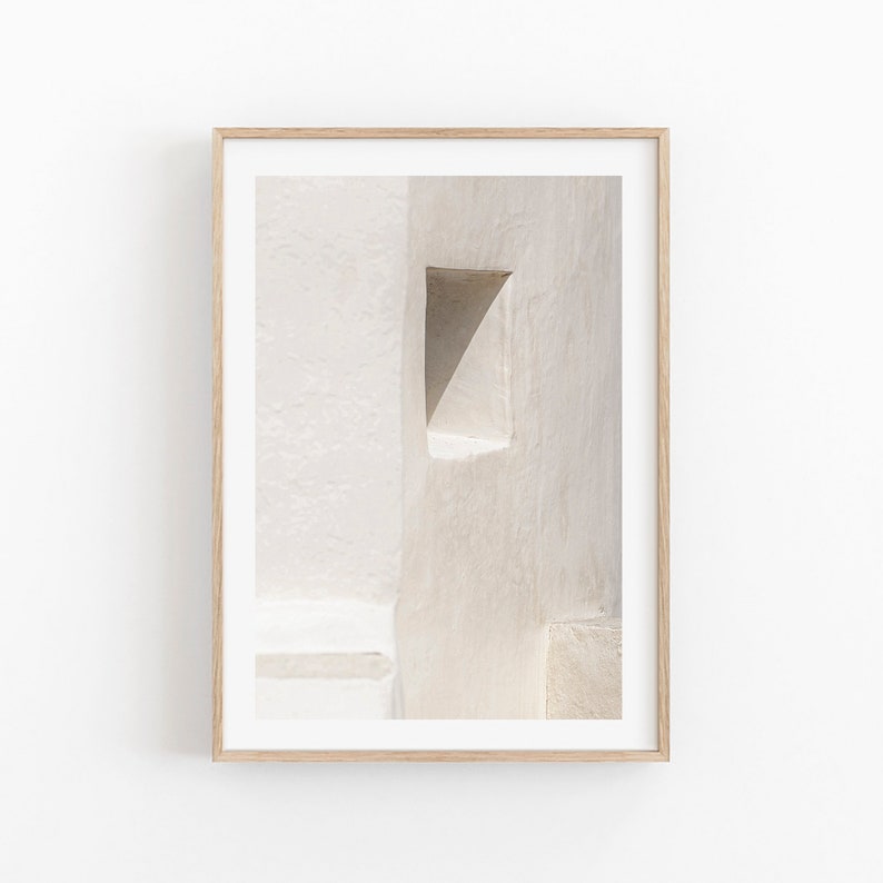 May include: Framed art print depicting an abstract architectural detail. The image shows a textured, off-white wall with a triangular opening. The artwork is presented in a light-coloured wooden frame, suitable for minimalist decor.