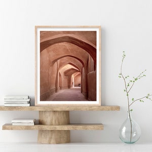 May include: A photograph of a long, narrow hallway with arched ceilings. The walls are a warm, reddish-brown color, and the floor is a light brown. The hallway is empty, except for a few shadows.