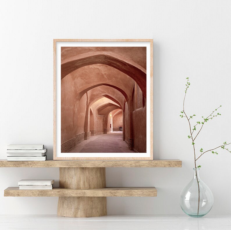 May include: A photograph of a long, narrow hallway with arched ceilings. The walls are a warm, reddish-brown color, and the floor is a light brown. The hallway is empty, except for a few shadows.