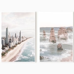 May include: Two framed prints of coastal scenes. The left print shows a city skyline with tall buildings along a sandy beach with blue ocean waves. The right print shows a rocky coastline with large rock formations in the ocean.
