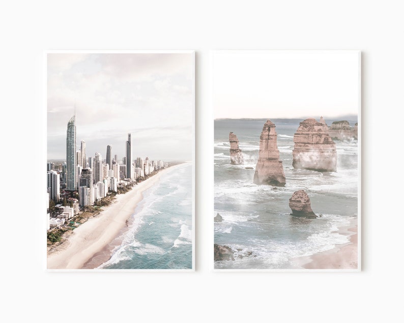 May include: Two framed prints of coastal scenes. The left print shows a city skyline with tall buildings along a sandy beach with blue ocean waves. The right print shows a rocky coastline with large rock formations in the ocean.