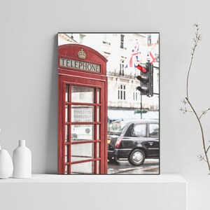 May include: A red telephone booth with the word "TELEPHONE" on the front, located on a street in London, England.  The booth is in front of a black taxi cab and a traffic light.