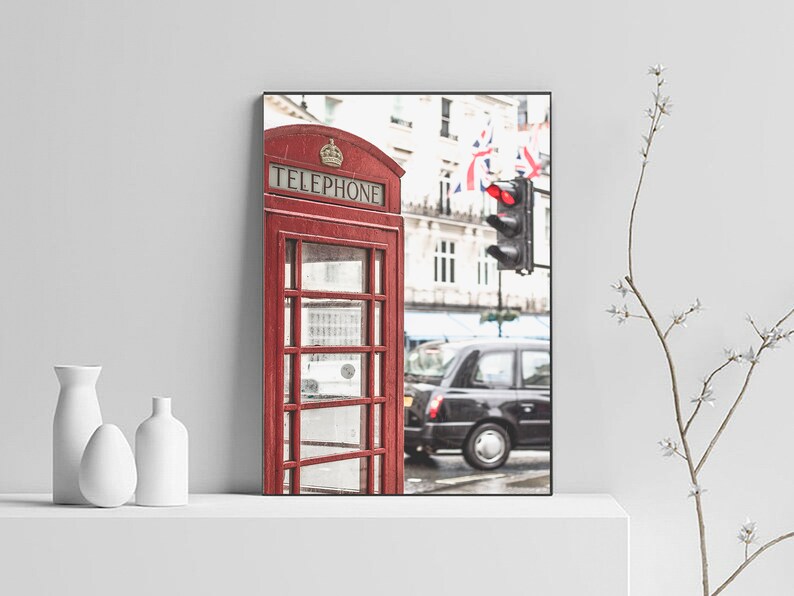 May include: A red telephone booth with the word "TELEPHONE" on the front, located on a street in London, England.  The booth is in front of a black taxi cab and a traffic light.