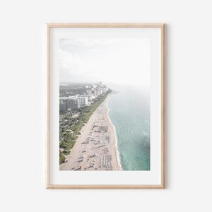 Pode incluir: Fotografia a&eacute;rea emoldurada de uma praia com &aacute;gua turquesa e uma costa arenosa ladeada por edif&iacute;cios. A imagem &eacute; em um estilo leve e arejado, com foco suave no horizonte. A moldura &eacute; de cor de madeira clara.