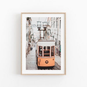 May include: A yellow and white vintage tram travels up a cobblestone street in Lisbon, Portugal. The tram is surrounded by buildings with colorful graffiti.