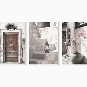 May include: A set of three prints featuring a weathered wooden door, a stone staircase with an old lantern, and a potted pink flowering plant against a white wall.