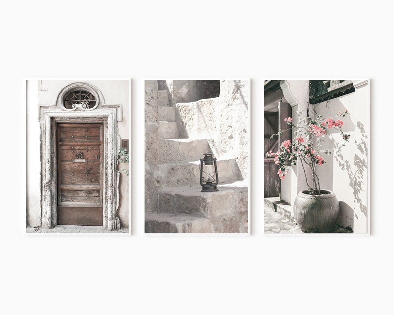 May include: A set of three prints featuring a weathered wooden door, a stone staircase with an old lantern, and a potted pink flowering plant against a white wall.