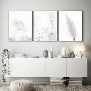 May include: Three minimalist black framed prints with white backgrounds and delicate floral and feather imagery. The prints are hung on a white wall above a white cabinet with a white countertop and a stack of books on either side.