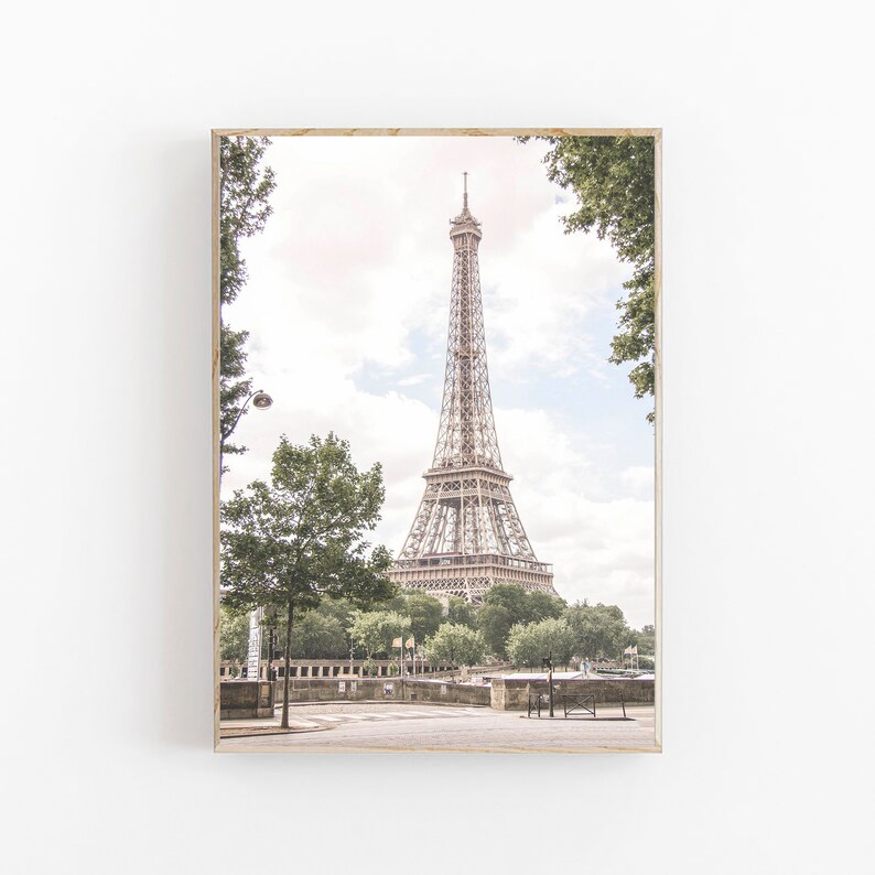 May include: A view of the Eiffel Tower in Paris, France. The tower is a metal structure with a light brown color. The tower is surrounded by trees and a street. The sky is a light blue color with some clouds.