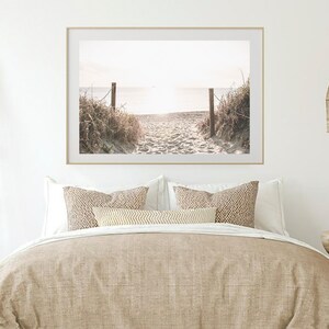 May include: A framed photograph of a sandy beach path leading to the ocean. The path is lined with tall grasses and the ocean is in the distance. The photo is in a light wood frame.