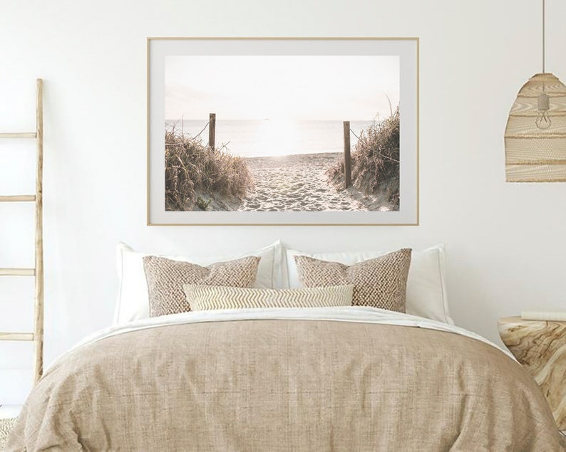 May include: A framed photograph of a sandy beach path leading to the ocean. The path is lined with tall grasses and the ocean is in the distance. The photo is in a light wood frame.