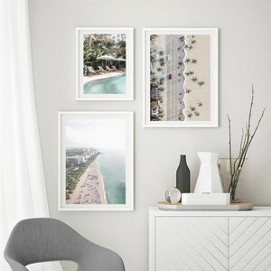May include: Three framed photographs of aerial views of a beach with palm trees, a swimming pool, and a city skyline.