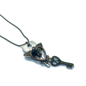 Puede incluir: Un collar con un colgante en forma de corazón de bronce, compuesto por una llave plateada con una gema negra y alas de bronce.