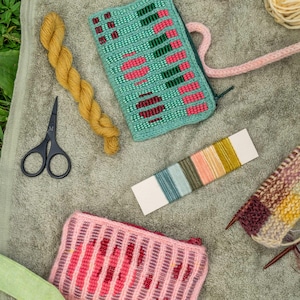 May include: Two rectangular zippered pouches featuring intricate knit patterns in mint green with pink and dark green accents, and a soft pink with deep red vertical stripes. Includes a skein of mustard yarn, black scissors, and a color sample card.