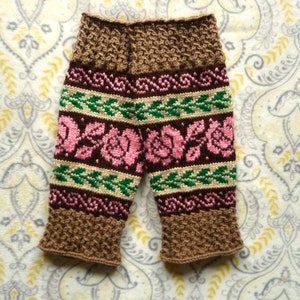 May include: Brown knitted baby pants with a pink and green floral pattern.