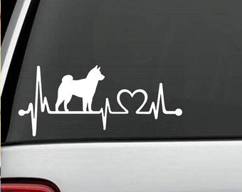 May include: White vinyl decal of a Shiba Inu dog silhouette with a heart beat line and a heart in the middle. The decal is on a gray car window.