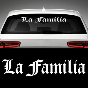 Könnte beinhalten: Weißer Vinyl-Autoaufkleber mit den Worten "La Familia" in gotischer Schrift. Der Aufkleber wird auf der Heckscheibe eines weißen Autos gezeigt. Der Text ist in einer fetten, stilisierten Schriftart.