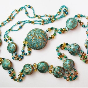 May include: A turquoise and gold necklace with large, round, patterned beads and smaller crystal beads.