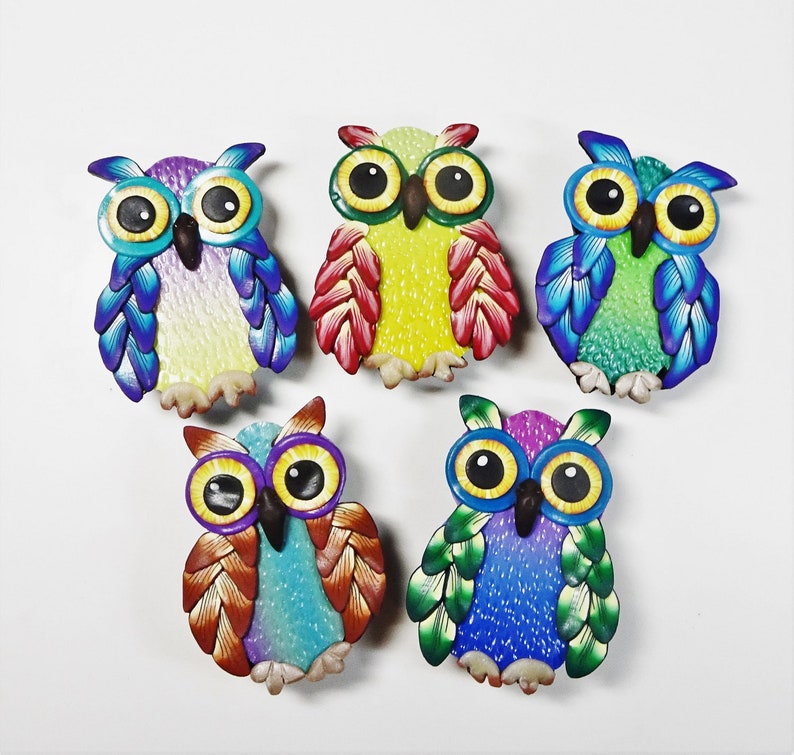 May include: Six colorful owl figurines made of polymer clay. Each owl has a different color scheme, including purple, yellow, green, blue, and brown. The owls have large, round eyes and are all facing forward.
