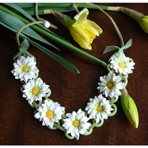 May include: A white daisy flower necklace with green leaves and white beads. The necklace is made of polymer clay and is a handmade piece of jewellery.
