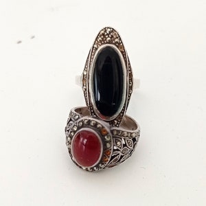 Puede incluir: Dos anillos de plata con piedras preciosas negras y rojas. Los anillos están decorados con intrincados diseños de filigrana.