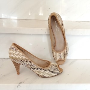 May include: A pair of beige woven peep-toe heels with a woven pattern. The heels are approximately 7.5 cm tall and have a brand label that says "Migato".