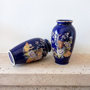 Könnte beinhalten: Zwei kleine blaue Keramikvasen mit goldenen Akzenten und Blumendesigns. Die Vasen sind mit goldenen Vögeln und Blumen verziert.