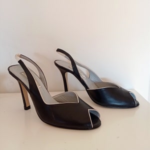 May include: A pair of black leather slingback heels with a white trim. The heels are open-toed and have a high stiletto heel.