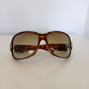 Puede incluir: Gafas de sol de carey con lentes marrones y detalles dorados.