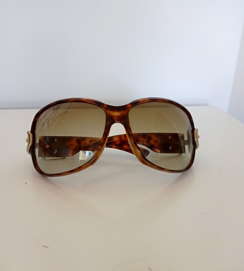 Puede incluir: Gafas de sol de carey con lentes marrones y detalles dorados.