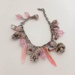 Peut inclure: Un bracelet en chaîne argent avec des breloques roses et brunes. Les breloques comprennent de petites perles roses, des breloques en forme de coquillages et de petites pierres.
