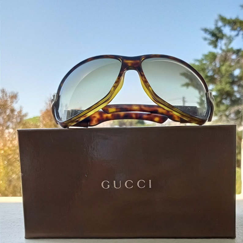 Puede incluir: Gafas de sol de carey con lentes marrones sobre una caja marr&oacute;n con la palabra "GUCCI" impresa en la parte delantera.
