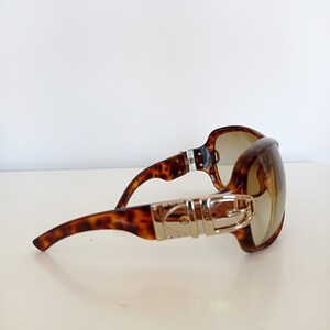 Puede incluir: Gafas de sol de carey con un detalle de hebilla plateada en el marco.
