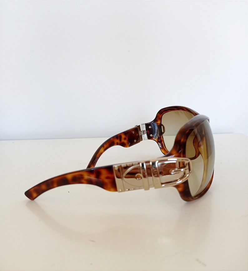 Puede incluir: Gafas de sol de carey con un detalle de hebilla plateada en el marco.