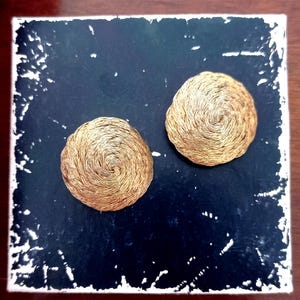 May include: Two gold-colored, round, coiled wire earrings. The earrings are on a black background.