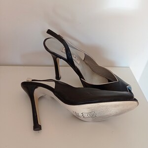 May include: A pair of black leather peep-toe heels with a slingback strap. The heels are high and have a thin stiletto.