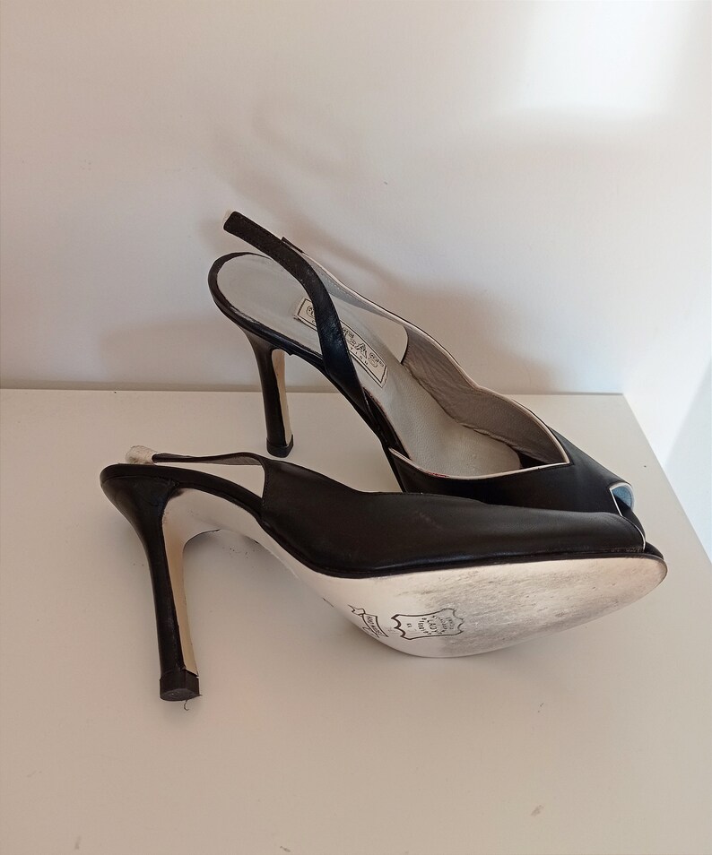 May include: A pair of black leather peep-toe heels with a slingback strap. The heels are high and have a thin stiletto.