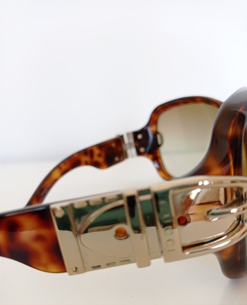 Puede incluir: Gafas de sol de carey con detalles dorados y un cierre de hebilla en el lateral.