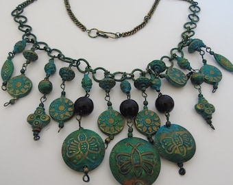 Puede incluir: Un collar artesanal con una cadena de bronce y colgantes turquesa y dorados. El collar presenta cuentas redondas y ovaladas, con un diseño de mariposa en los colgantes más grandes. El collar tiene un cierre de gancho.