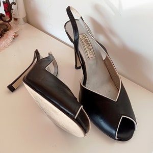 May include: A pair of black peep-toe heels with a white trim. The heels are made of leather and have a slingback strap. The shoes are labeled "GORE-TEX COLLECTION".