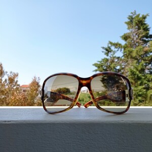 Puede incluir: Gafas de sol de carey con lentes marrones. Las gafas est&aacute;n sobre una superficie blanca.